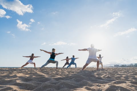 Diverse group holding warrior pose on beach